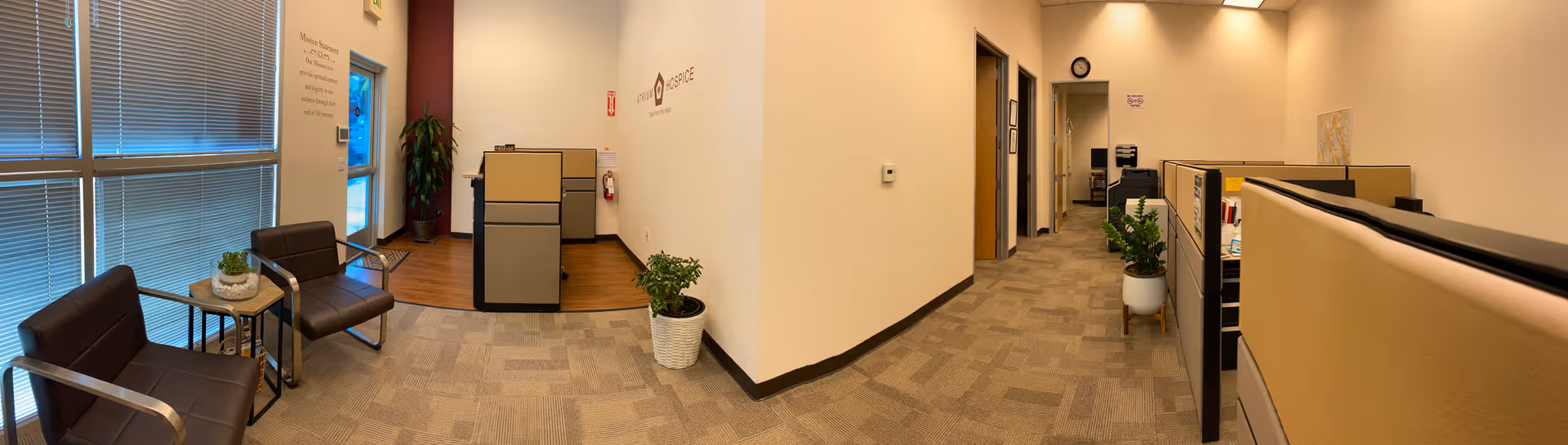 Atrium Hospice interior lobby with seating, cubicles, and potted plants.