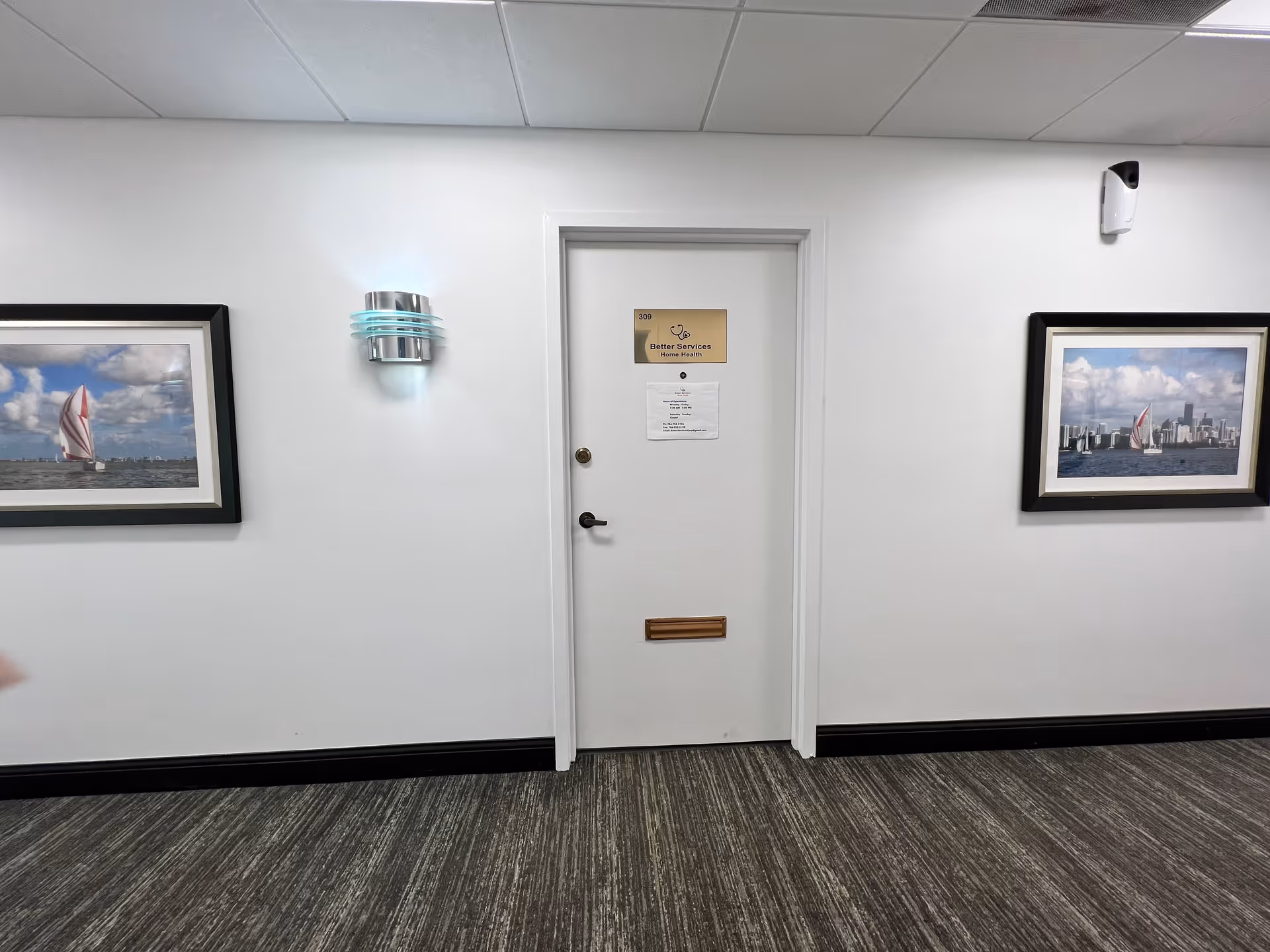 White interior hallway with framed sailboat photos on both sides and a central door.