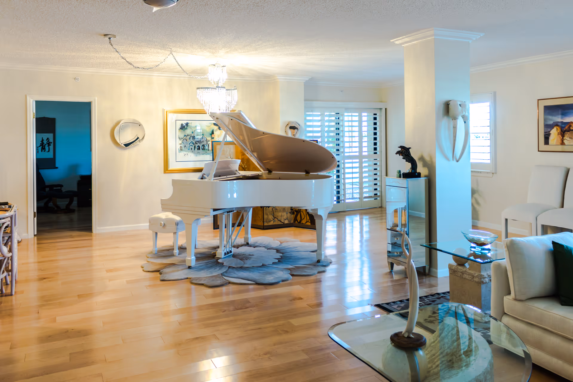 Bright living room with a white grand piano, chandelier, and airy seating area.