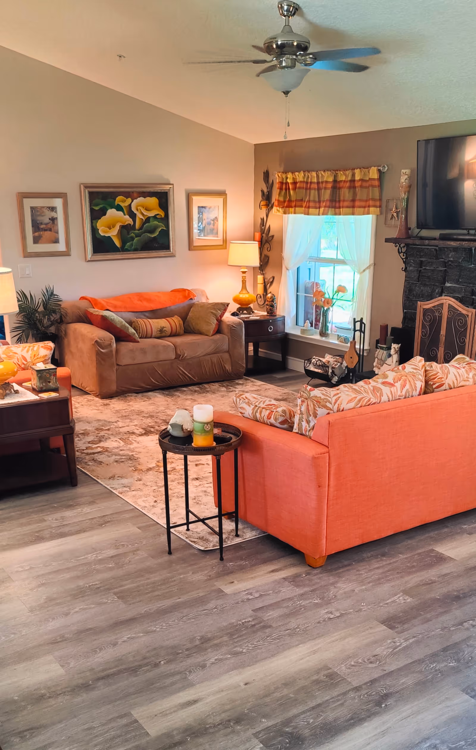 Cozy living room in a senior living facility with orange sofa, art, and a fireplace.