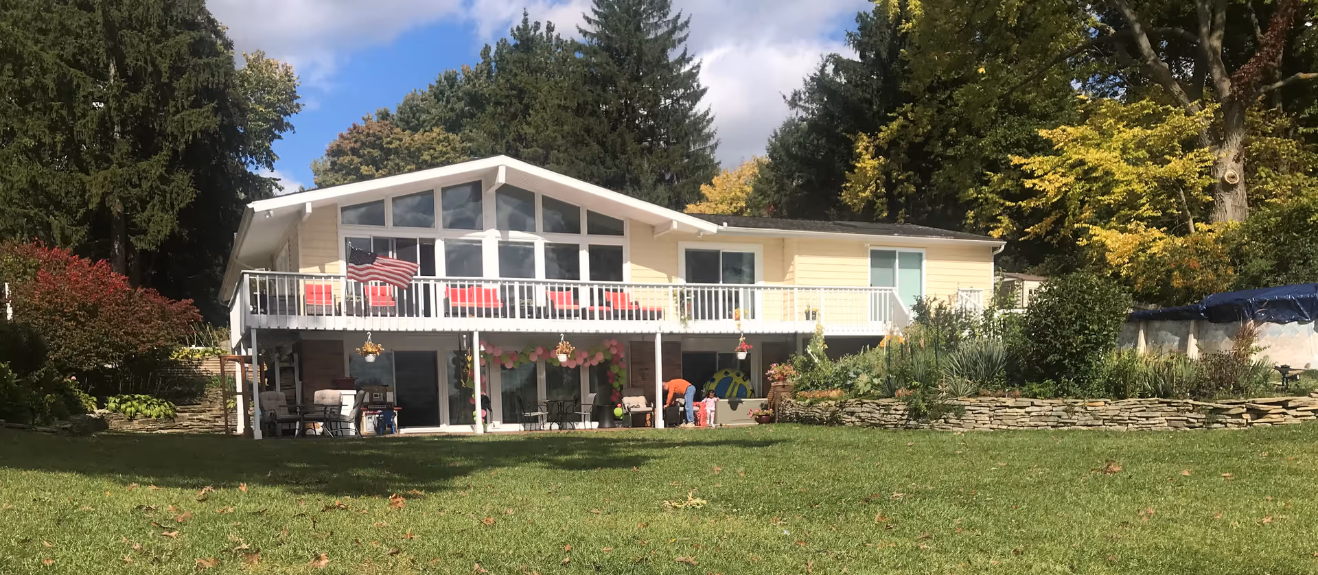 Two-story yellow senior living facility with a spacious front lawn, balcony, and outdoor seating.