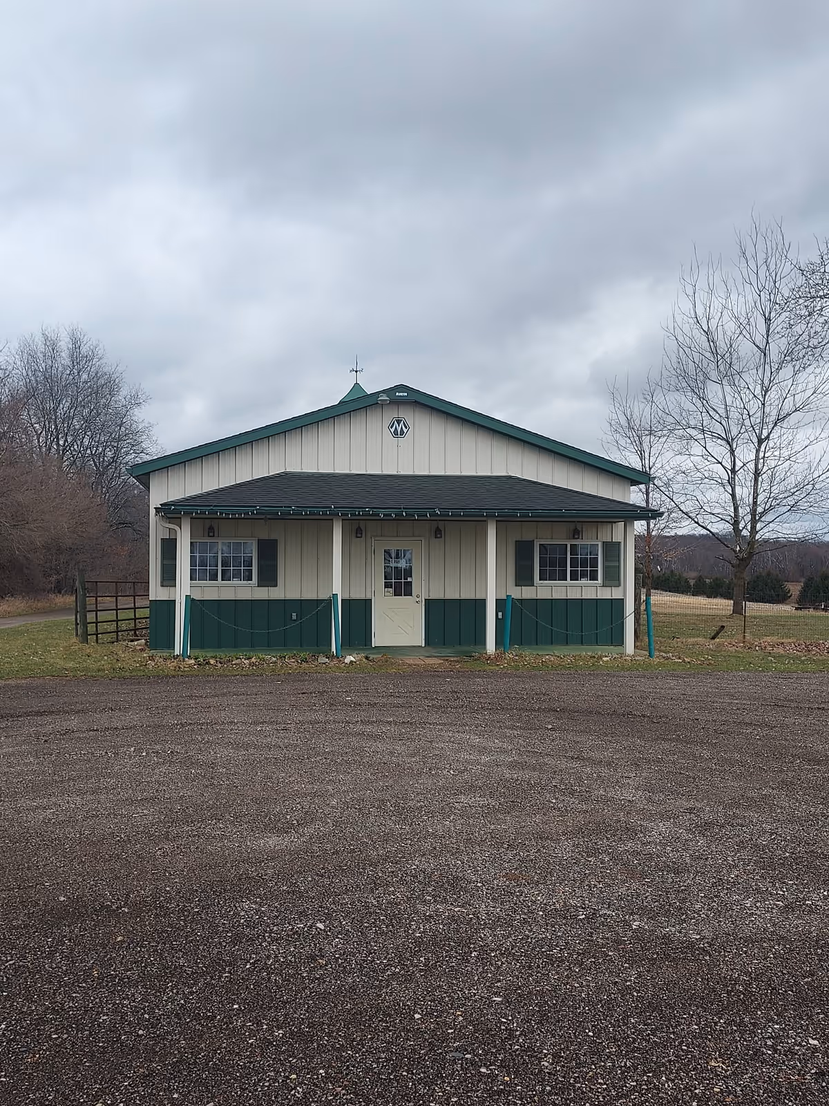 Small beige and green building with a front porch in a rural, empty lot.