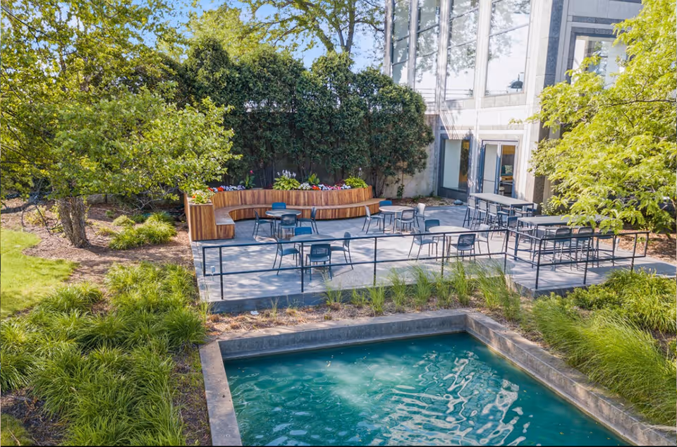 Outdoor patio area with chairs, tables, and a rectangular pool surrounded by greenery.