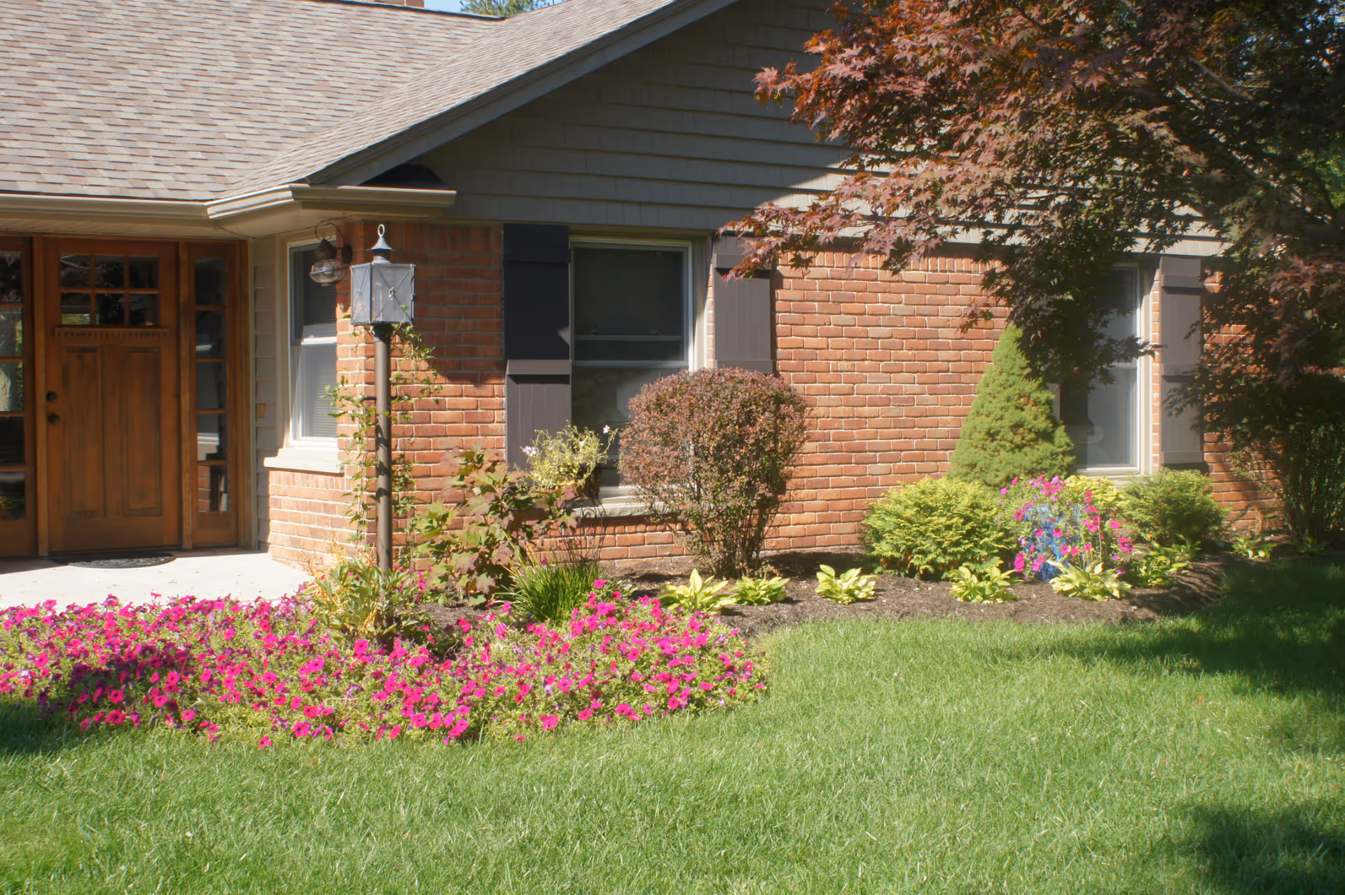 Front exterior of a brick senior living building with manicured lawn and colorful flowers.