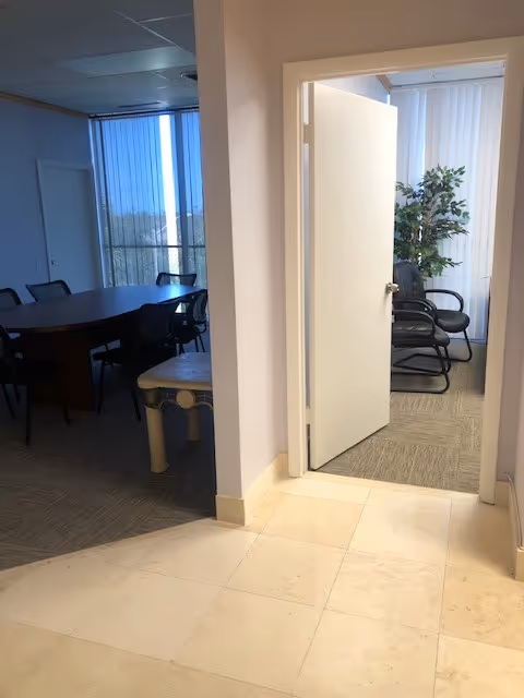 Interior hallway opening to a conference room with a table, chairs, and potted plant.