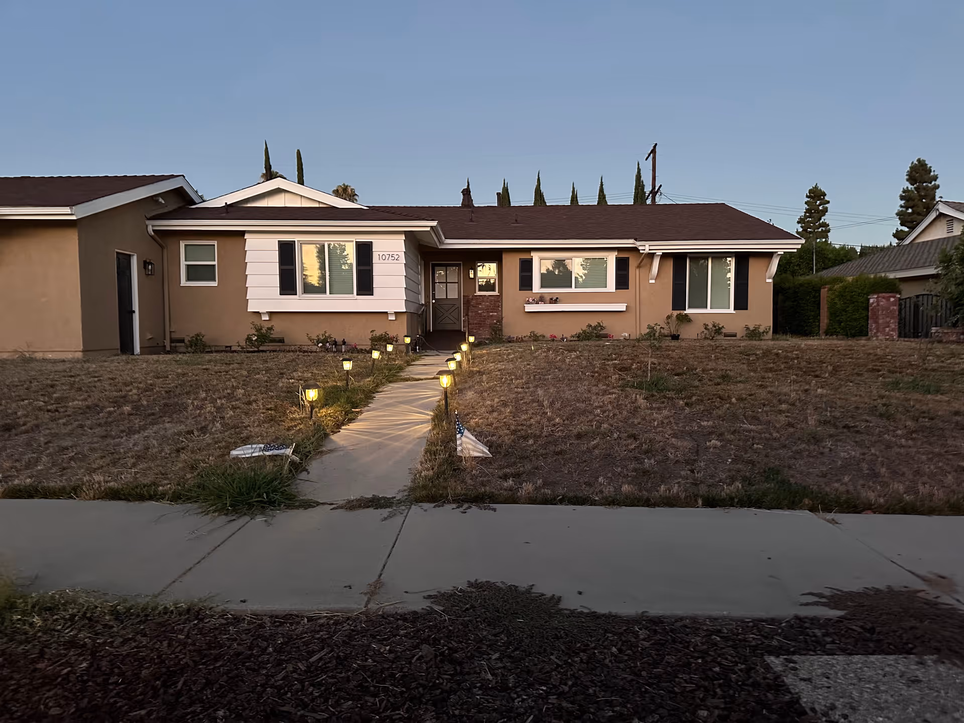 A single-story tan building with a walkway lined by yard lights to the front door.