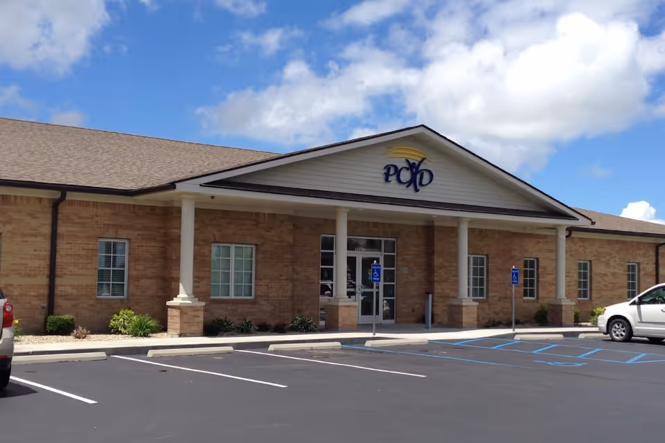 Front view of a brick health department building with columns and a parking lot.