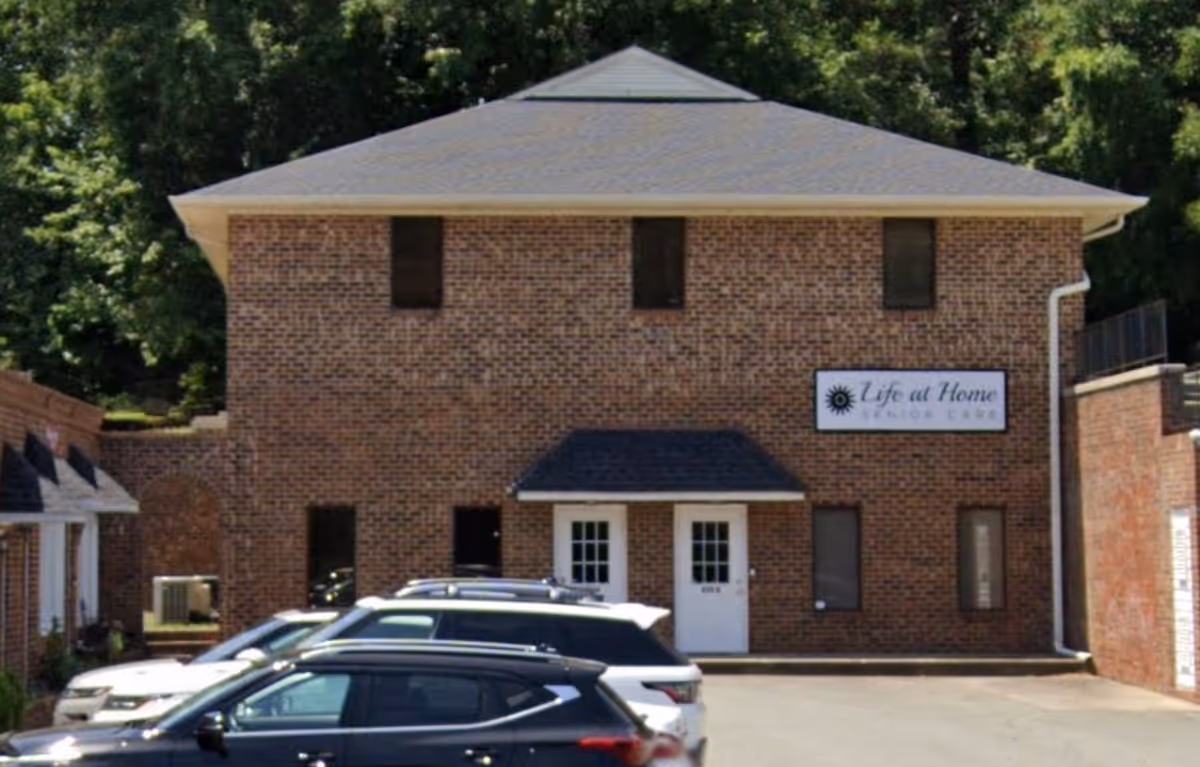 Brick two story senior care facility with parked cars and a visible Life at Home sign.