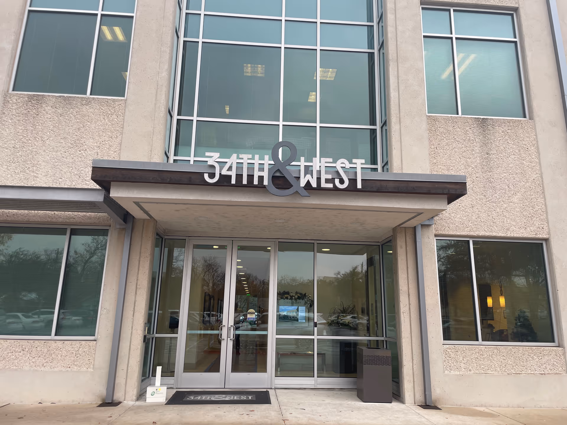 Front entrance of a modern building with large glass doors and 34th and West signage.