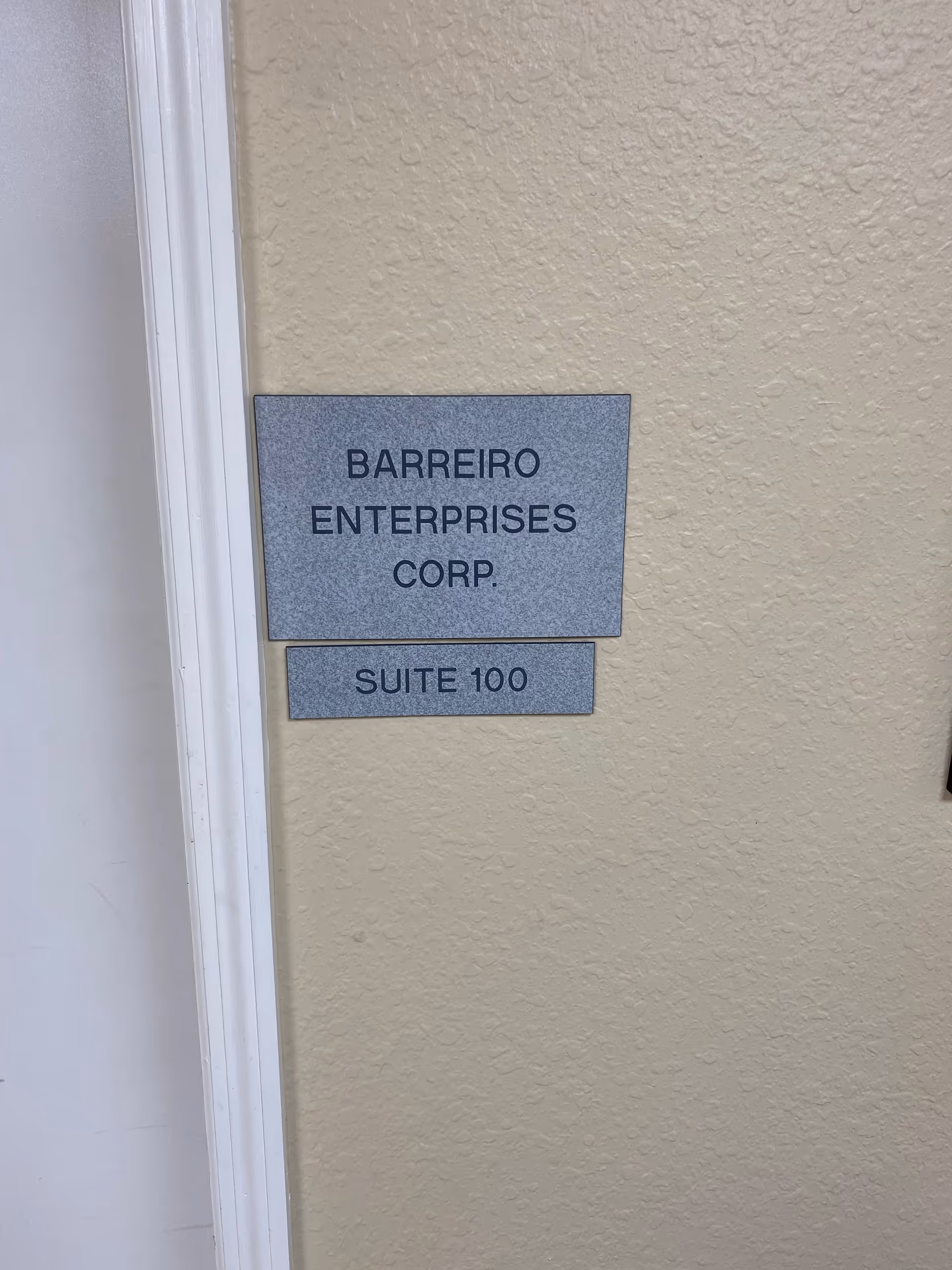 Two gray plaques on a beige wall read Barreiro Enterprises Corp., Suite 100.