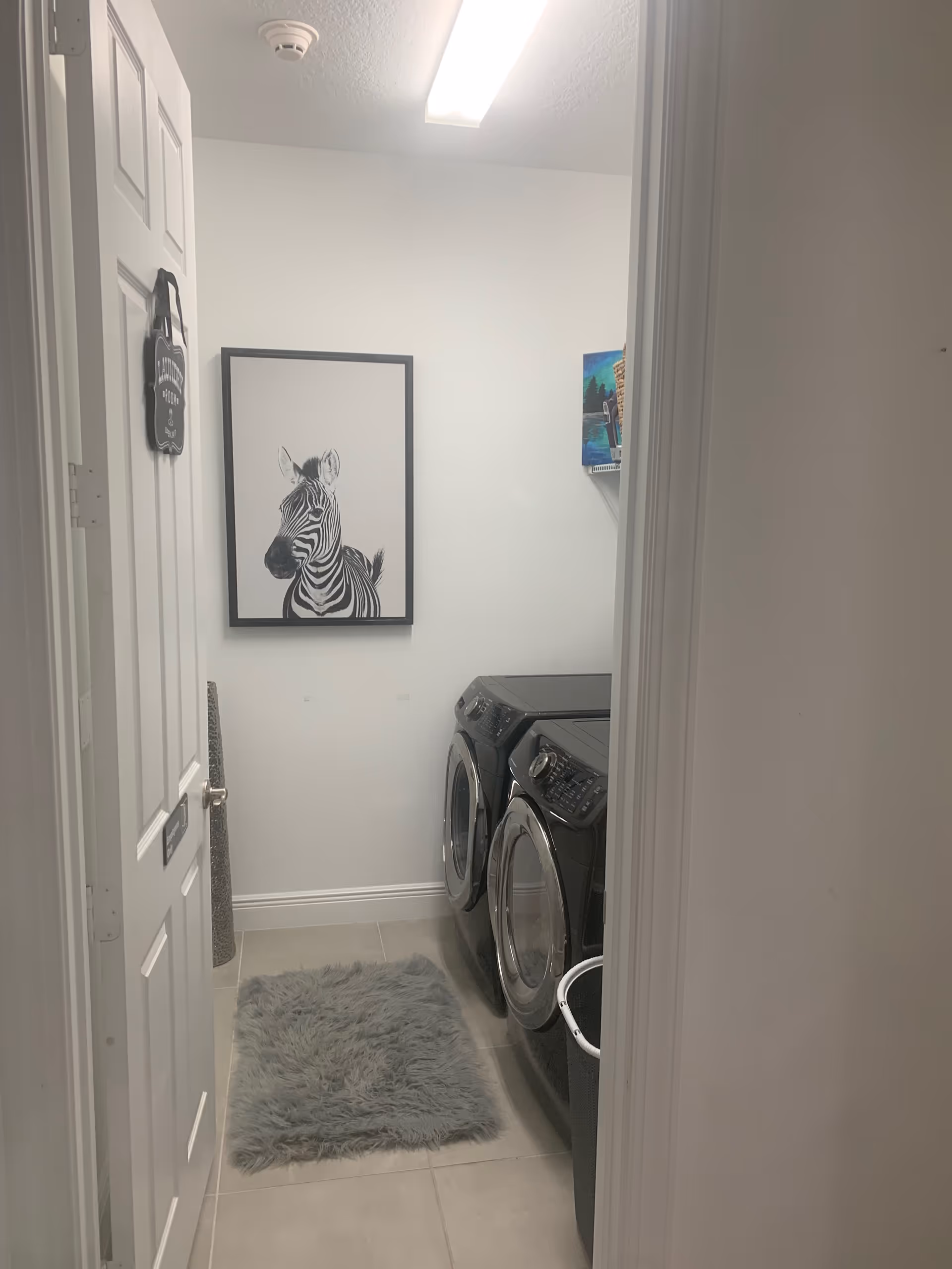 Narrow laundry room with front-loading washers, a gray rug, and zebra art on the wall.