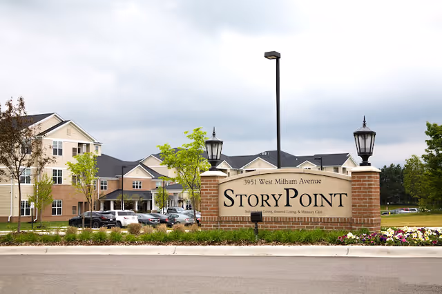 Stone entrance sign reading "StoryPoint" with the StoryPoint Portage building, landscaping, and parked cars behind it.
