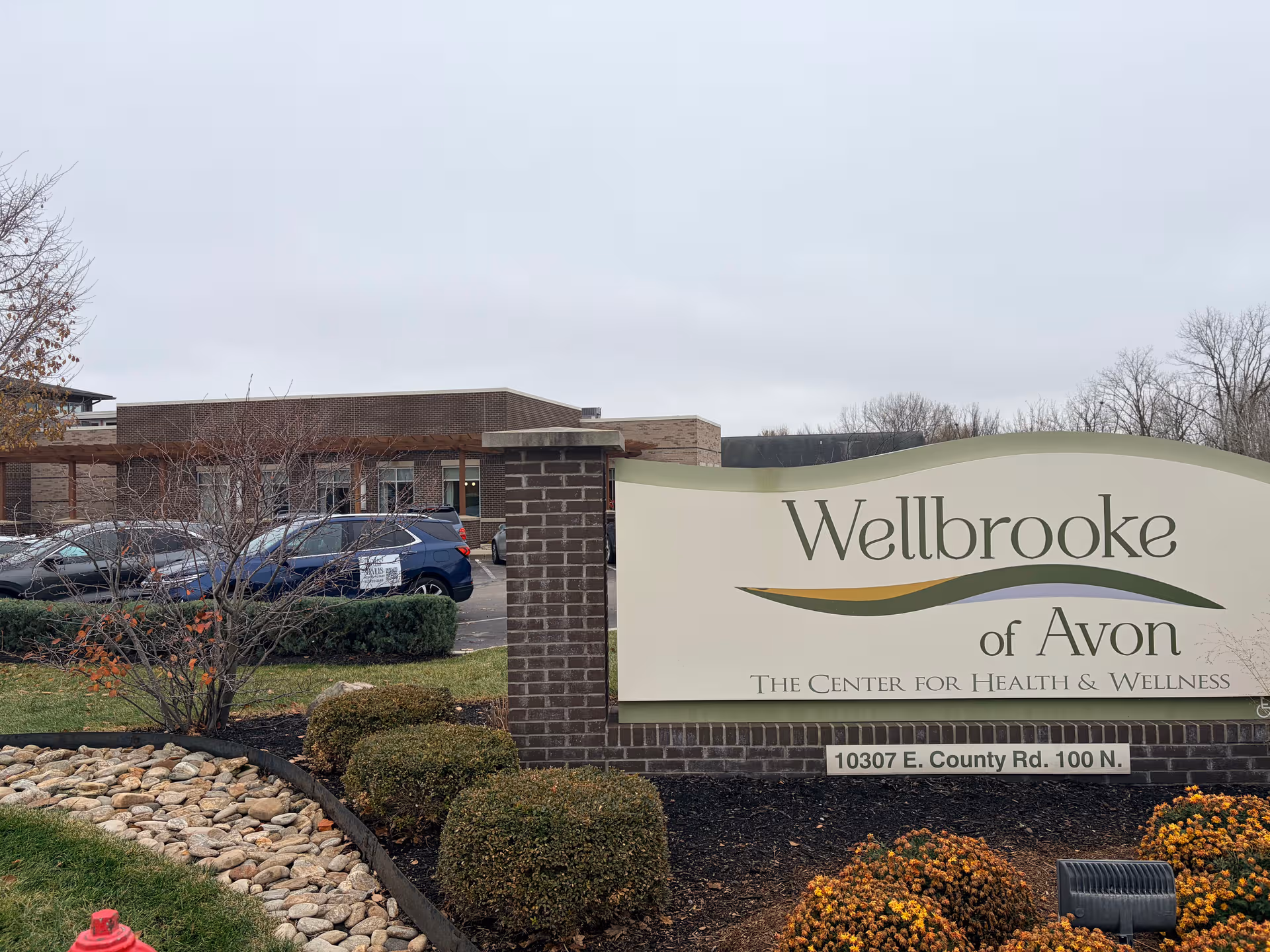 Wellbrooke of Avon entrance sign with brick base and parked cars nearby.