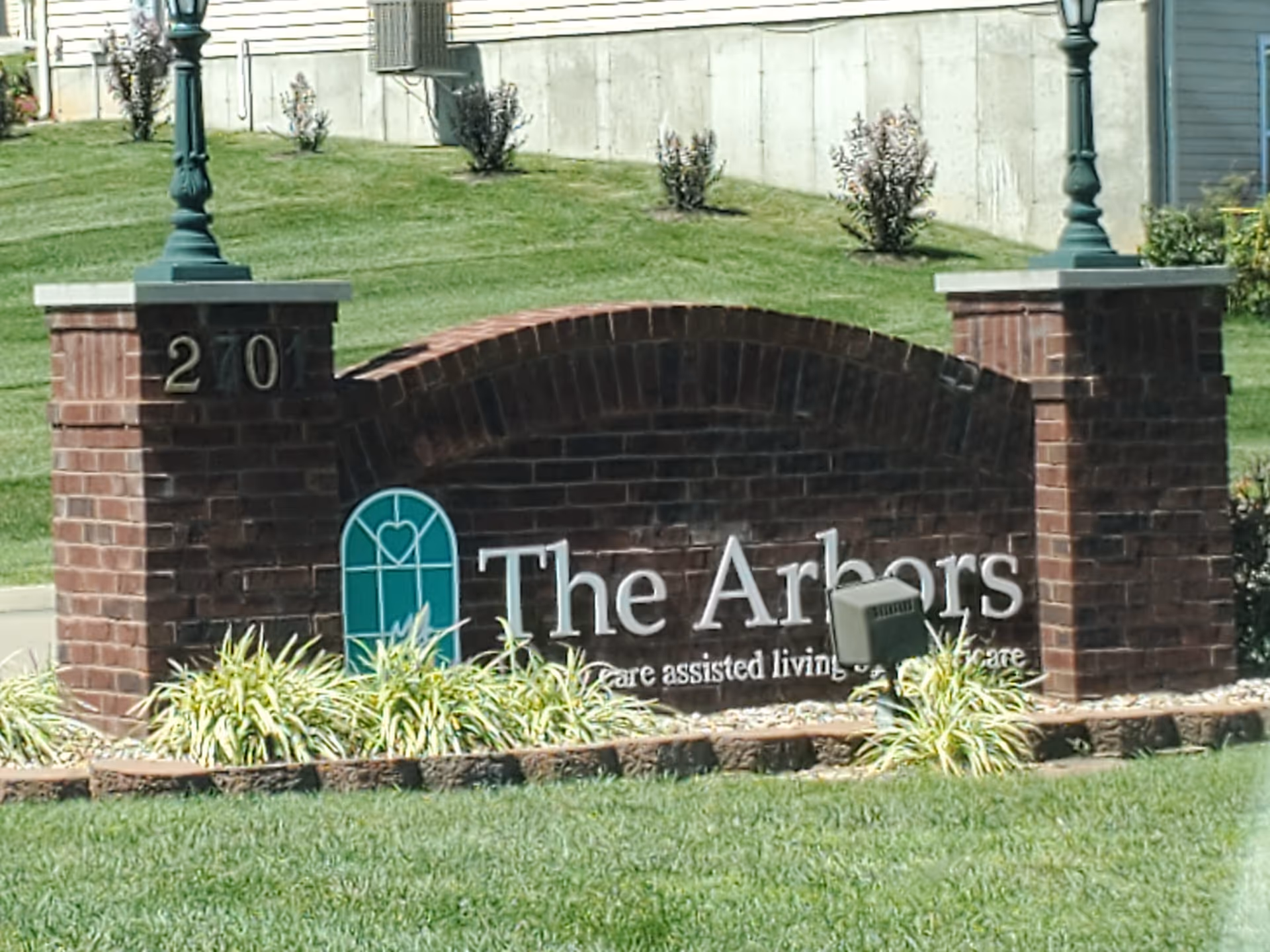 Brick entrance sign reads The Arbors with surrounding landscaped lawn