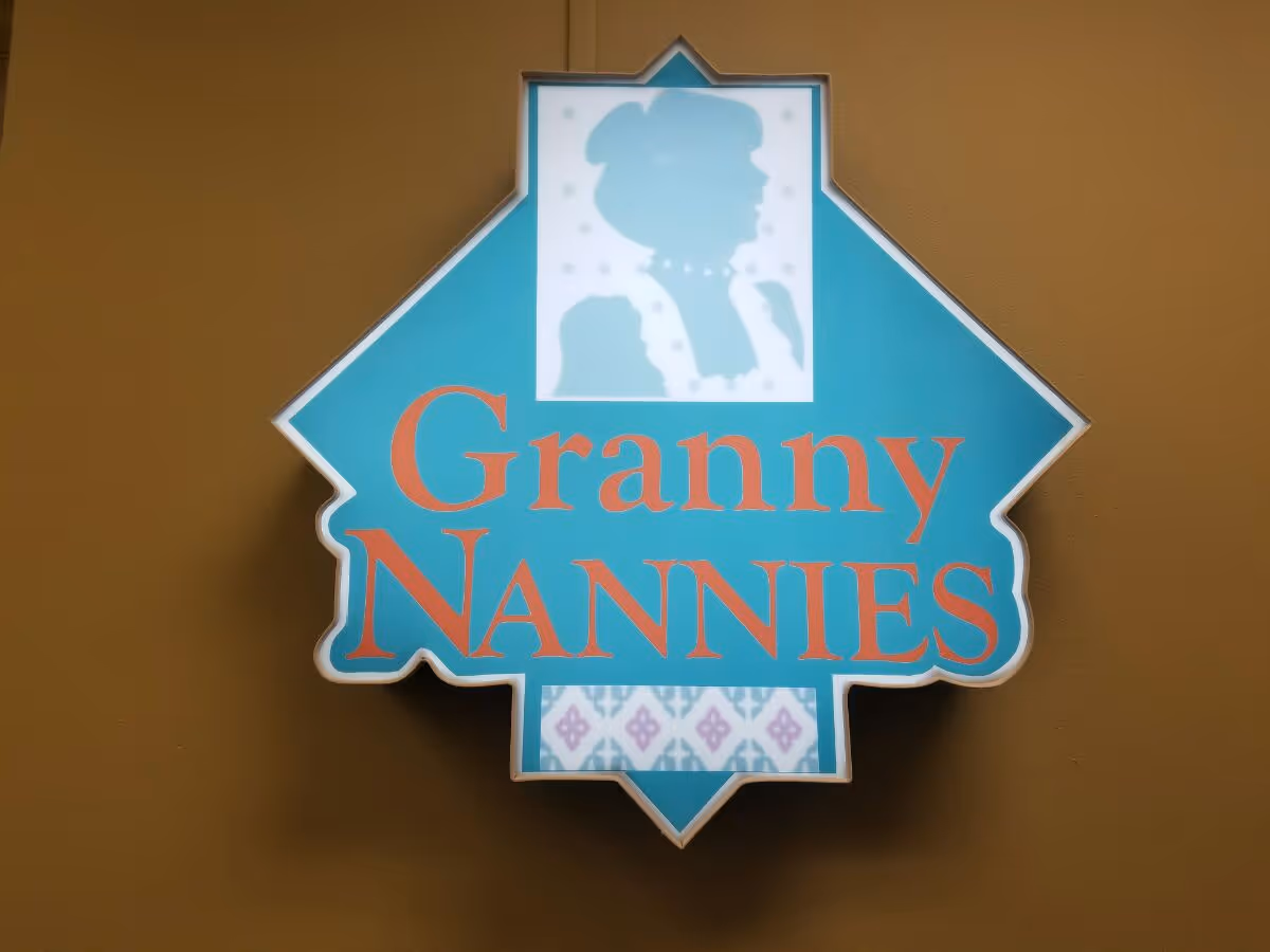 Blue badge-shaped sign reading Granny NANNIES mounted on a brown exterior wall.