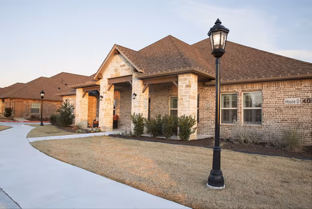 Single-story brick senior living building with a covered porch, walkway, and lamp posts.