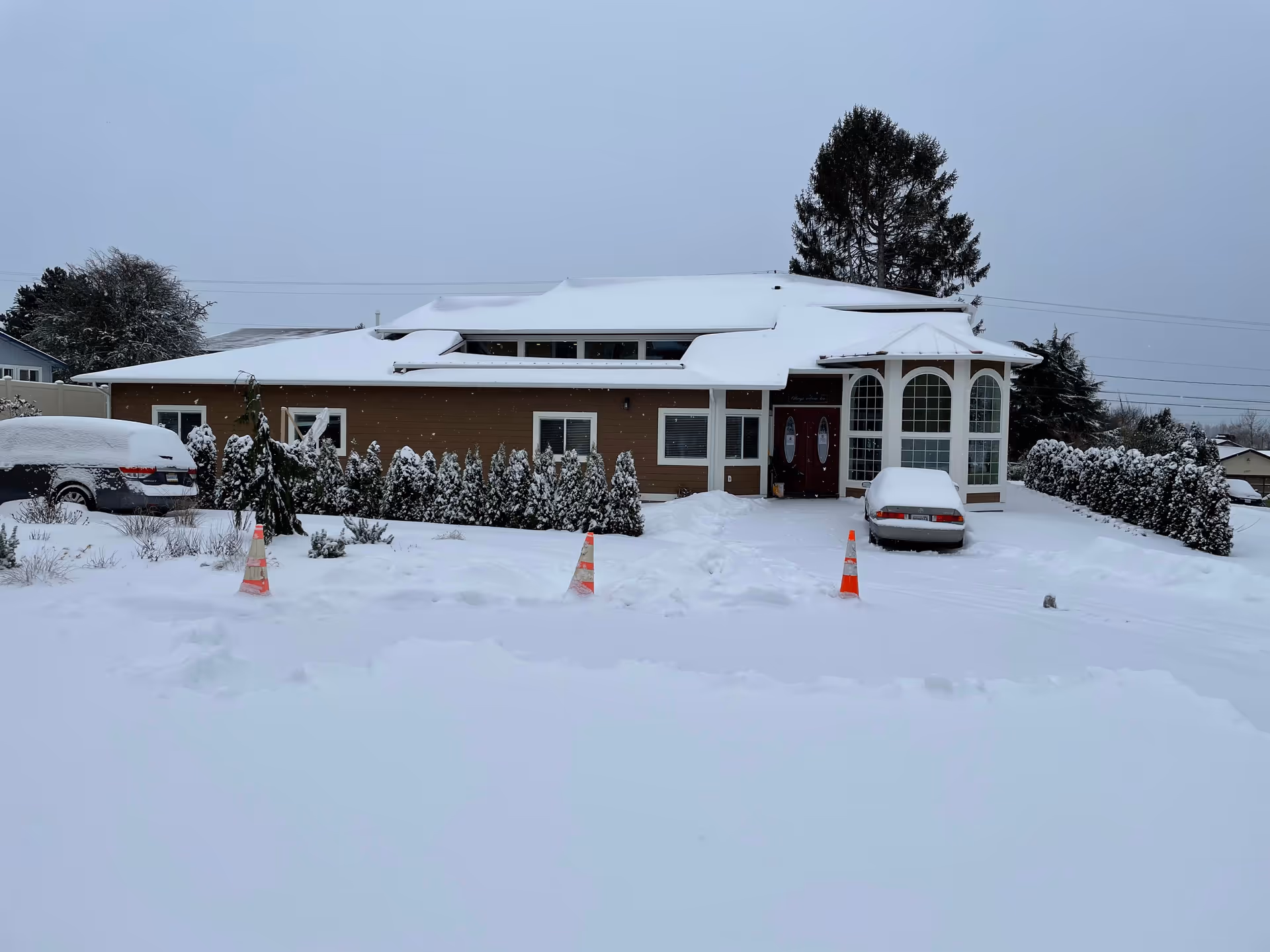 Snow covers a single-story facility with a curved glass entrance and parked cars.