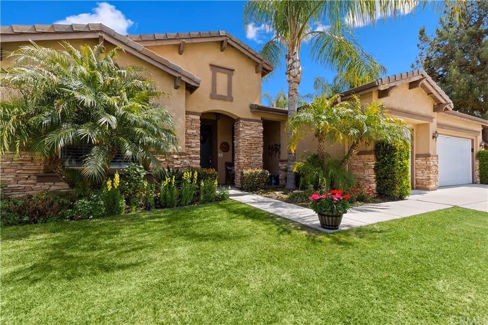Stone-accented senior living home with manicured lawn, tropical landscaping, and a two-car garage.