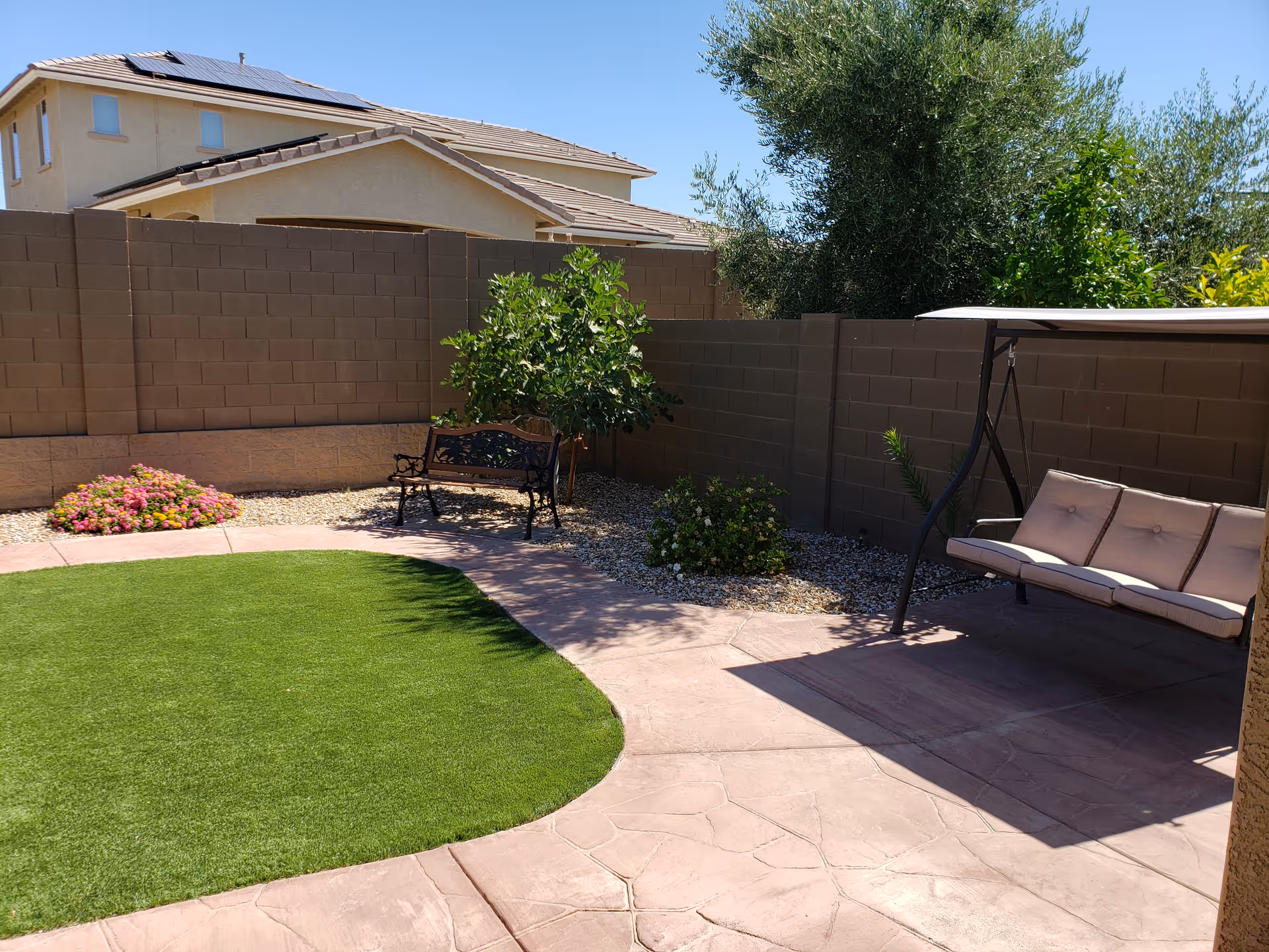 Outdoor backyard with lawn, bench, and cushioned swing along a brown brick wall.