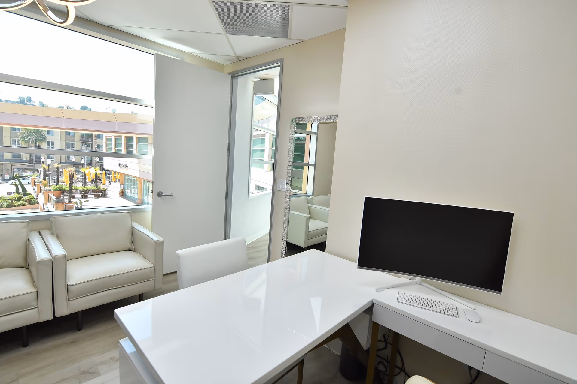 Bright modern office lobby with white desk, computer, and cream seating by a large window.