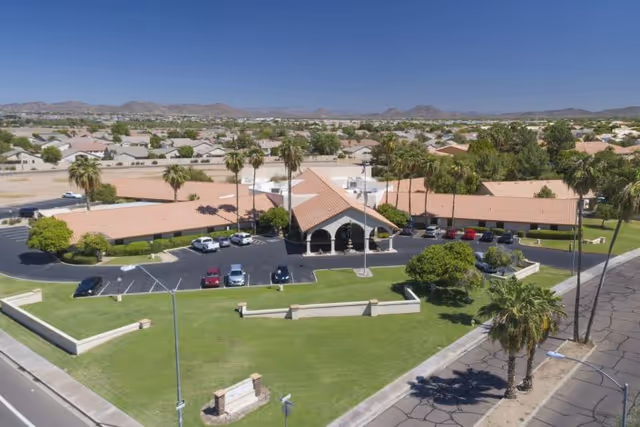 Aerial view of the Lake Pleasant Post Acute Rehabilitation Center showing the building entrance, parking lot, palm trees, and surrounding neighborhood under a clear blue sky.
