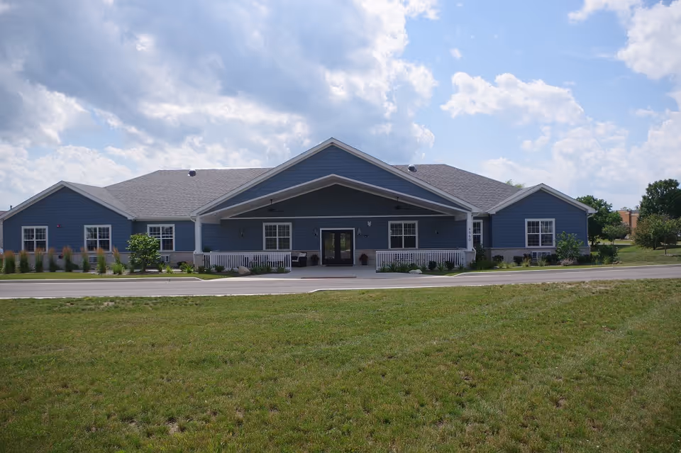 Blue single-story senior living facility with a central covered entrance and manicured lawn.