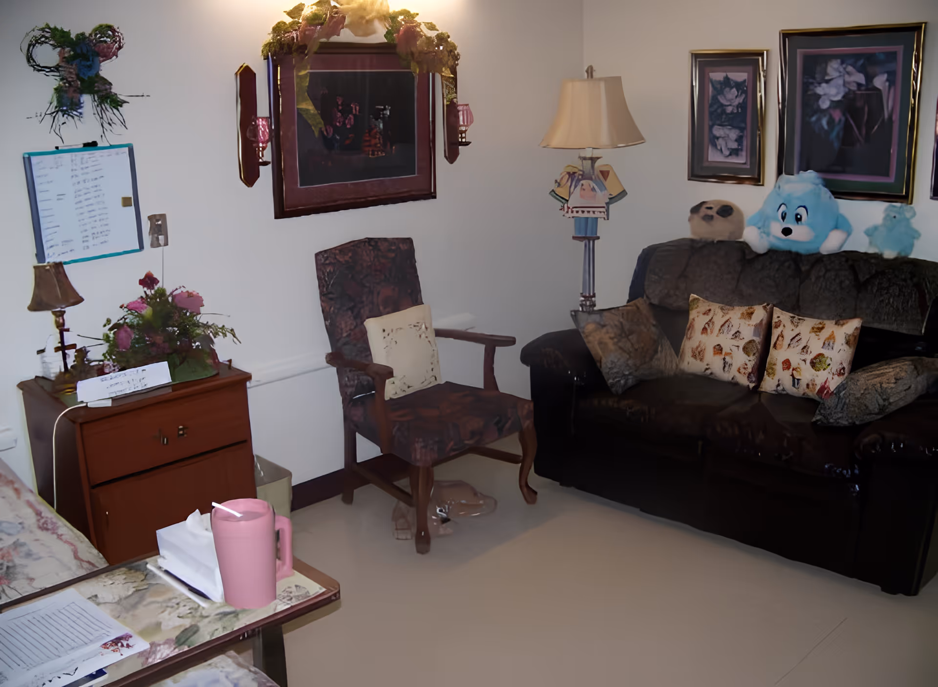 Cozy sitting area with a sofa, upholstered armchair, side table, lamp, framed wall art and small decorative items.