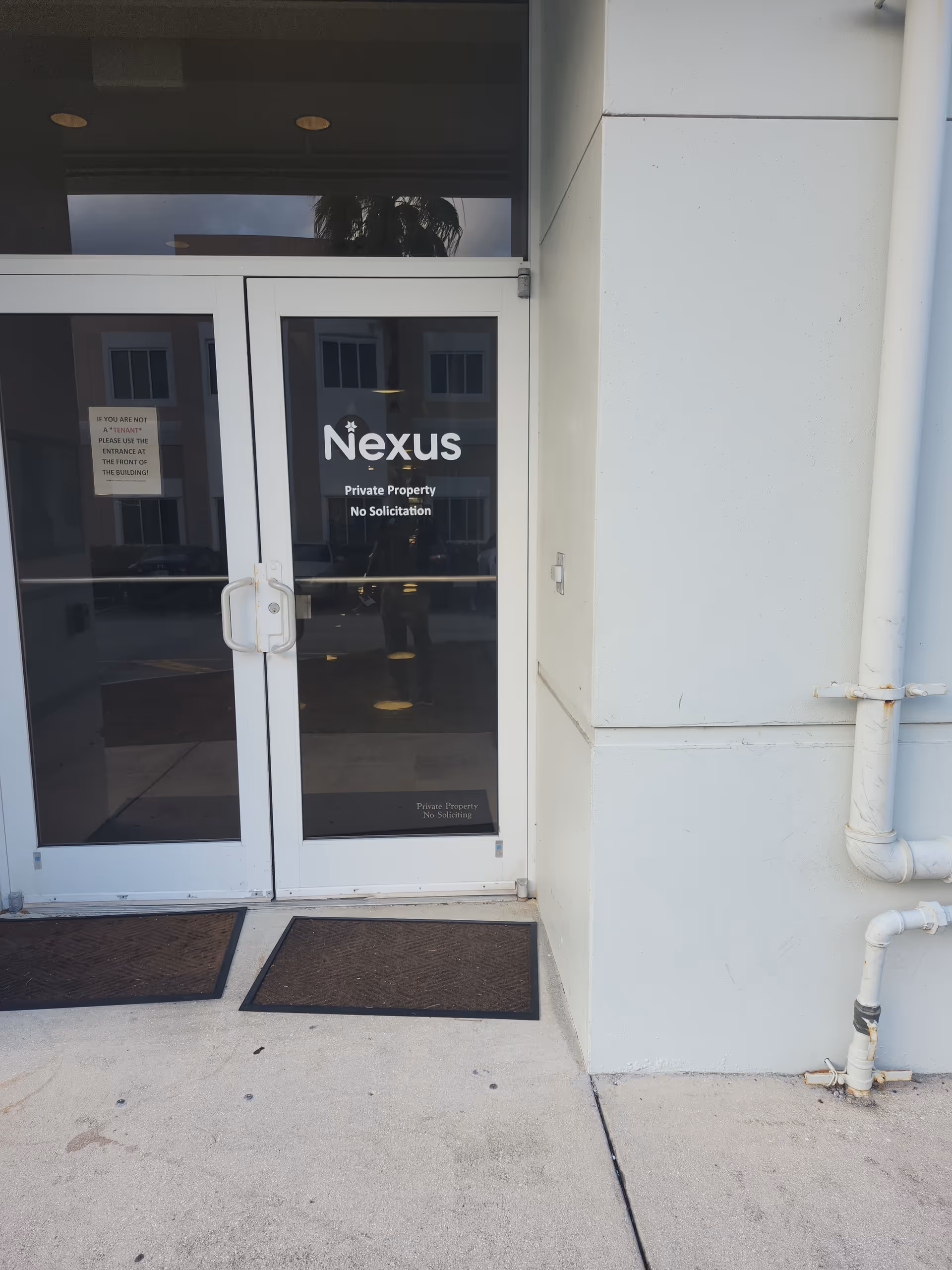 Glass entrance doors with Nexus sign, private property, no solicitation, building front.