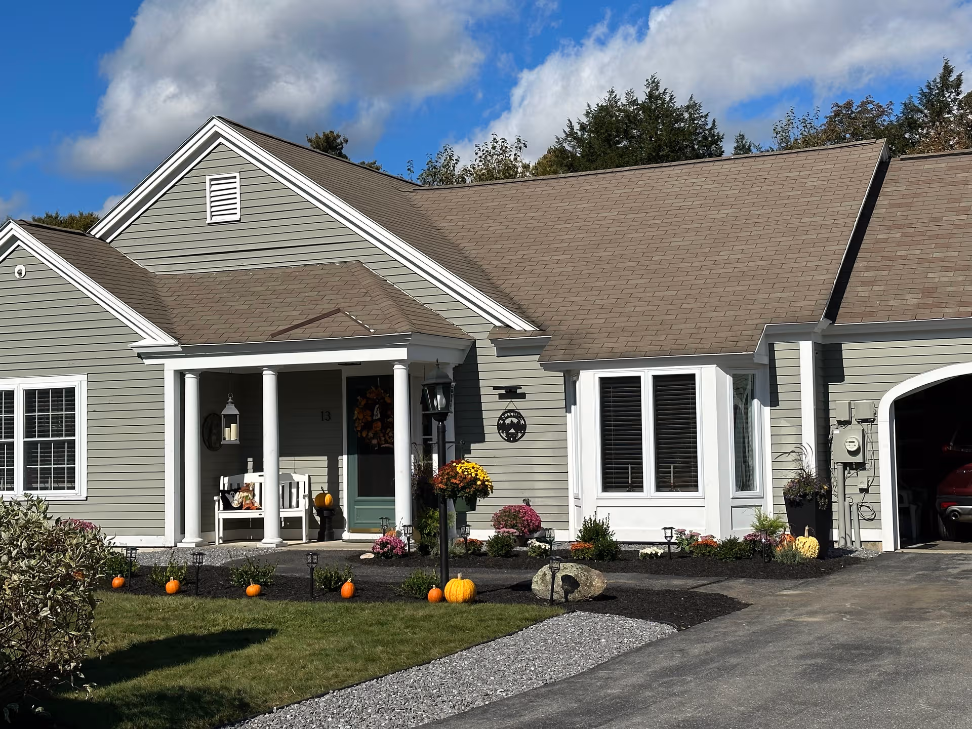 Gray senior living building with a front porch, pumpkins, and landscaped walkway under a blue sky