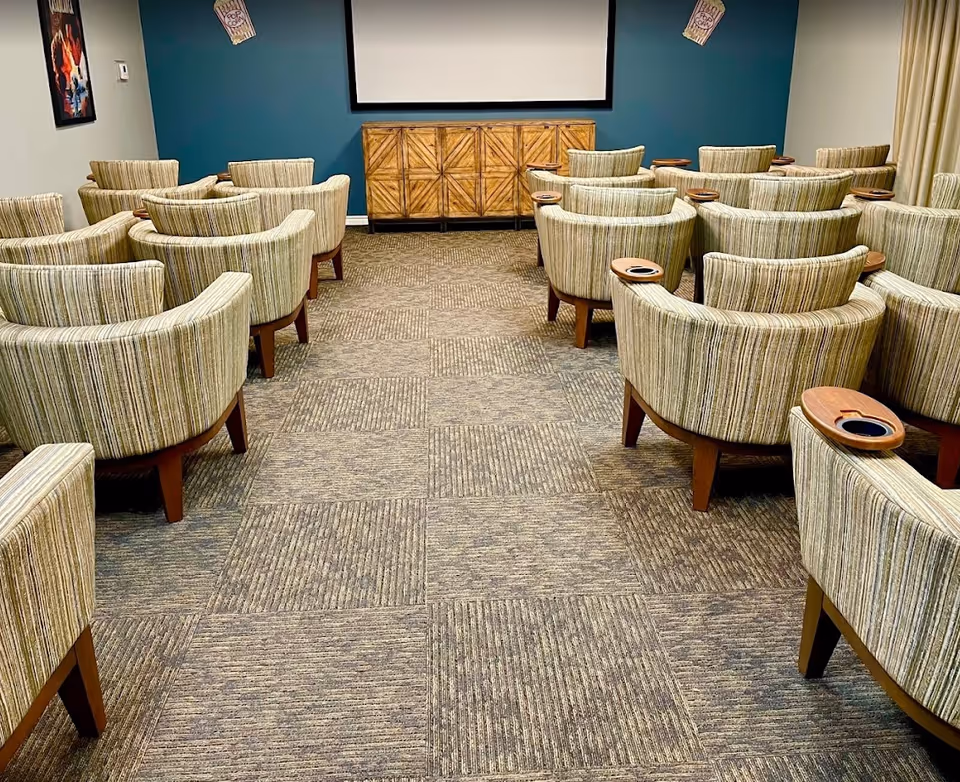 Small screening room with rows of striped upholstered armchairs facing a wall-mounted screen and wooden cabinet.