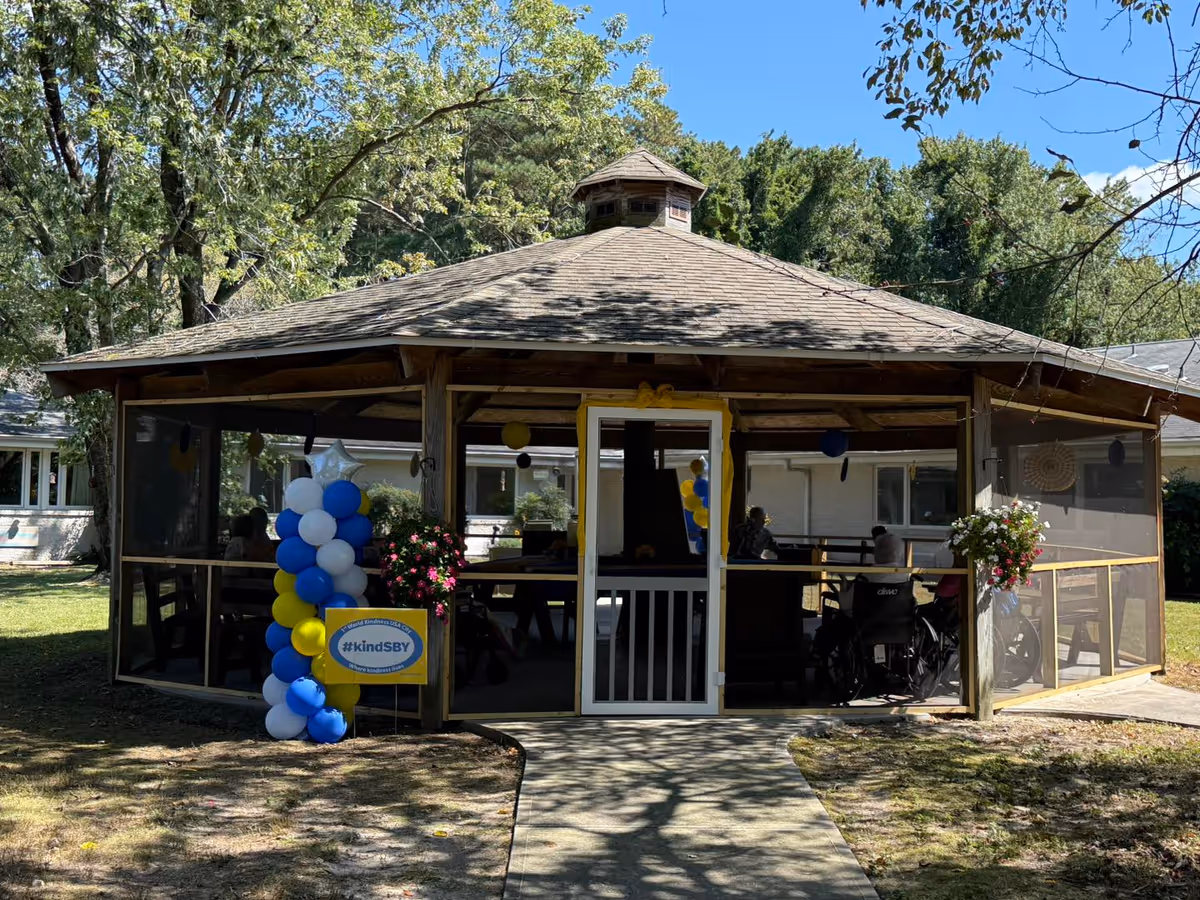 Outdoor screened pavilion at a nursing home with balloons and attendees.
