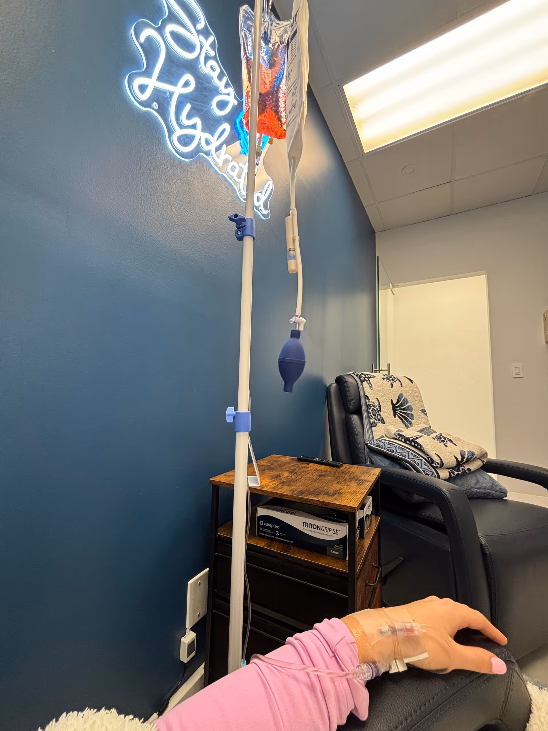Infusion chair beside blue wall with IV pole and patient arm visible.