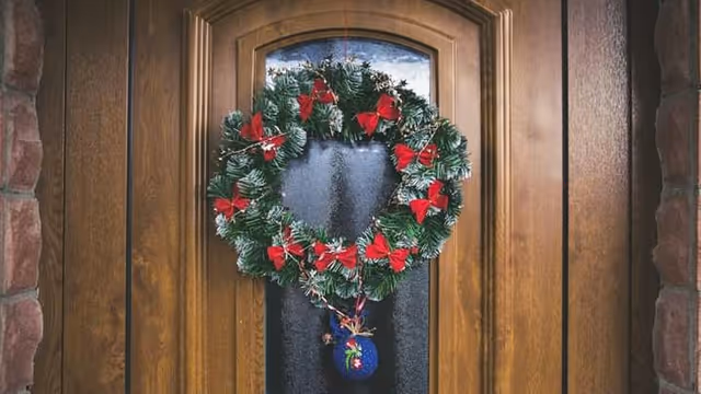 Wooden front door with festive wreath and red bows hanging outside.