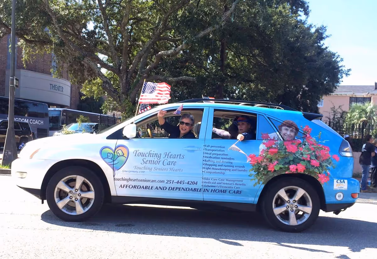 Blue Touching Hearts Senior Care promo car with people waving from windows and an American flag.