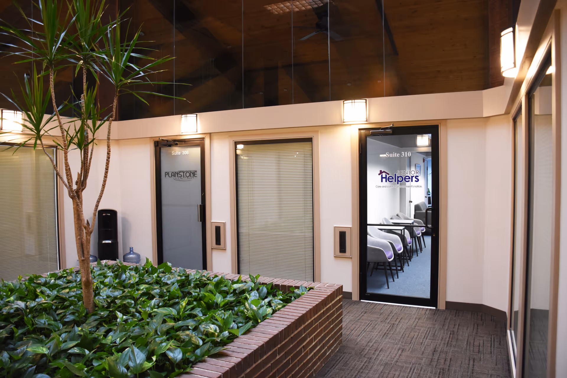 Interior hallway of a senior living facility with glass doors and a brick planter.