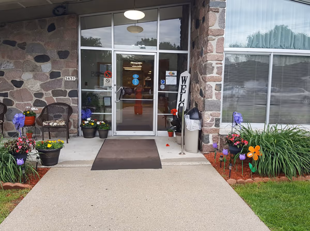 Stone facade entrance with glass doors, potted flowers, and a welcome sign.