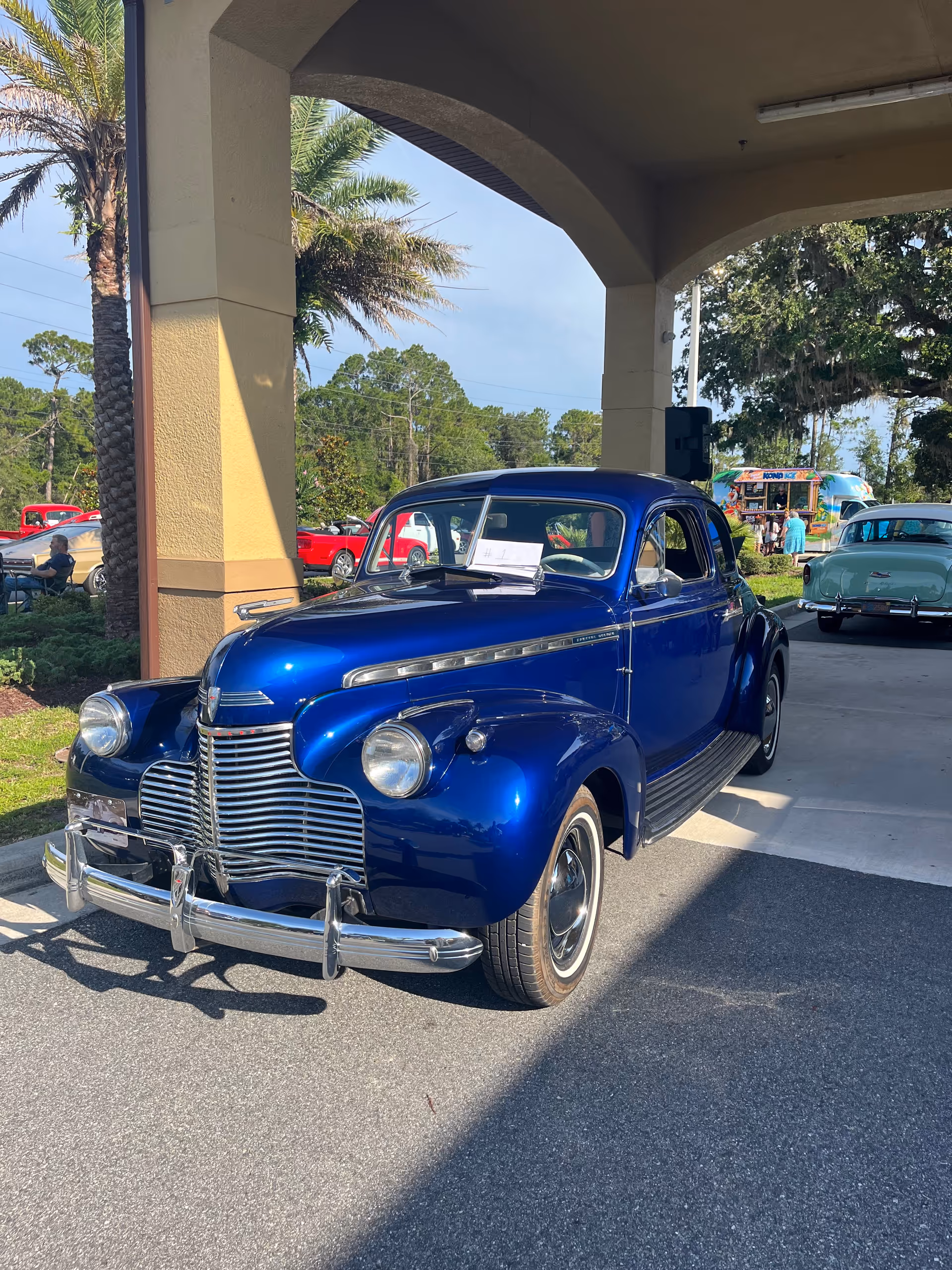 Shiny blue vintage car under a covered entrance at a senior facility's front exterior.