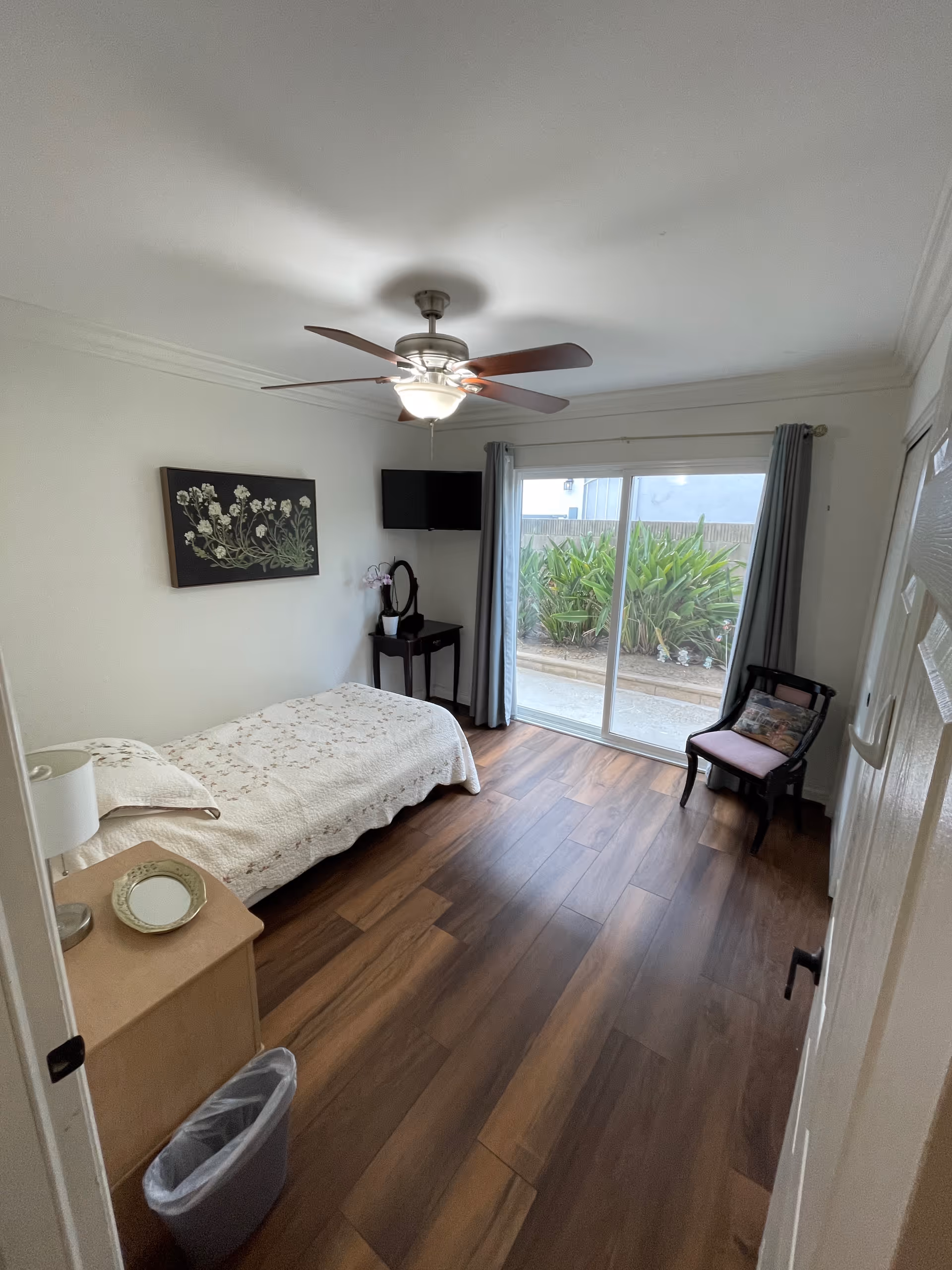 Cozy bedroom with single bed, TV, ceiling fan, and sliding glass door to outdoor space.
