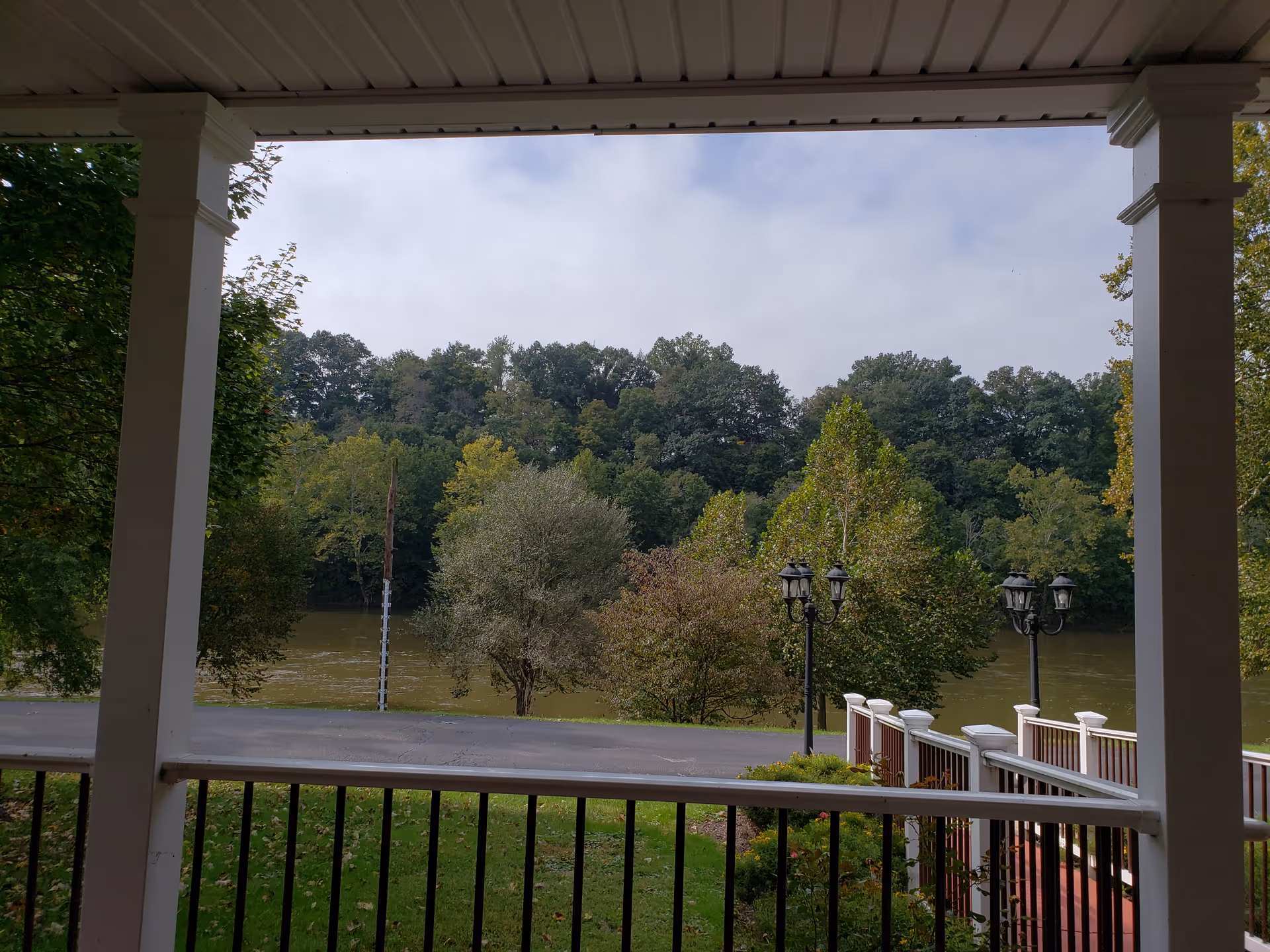 Covered porch view overlooking river, with trees and ornate street lamps.
