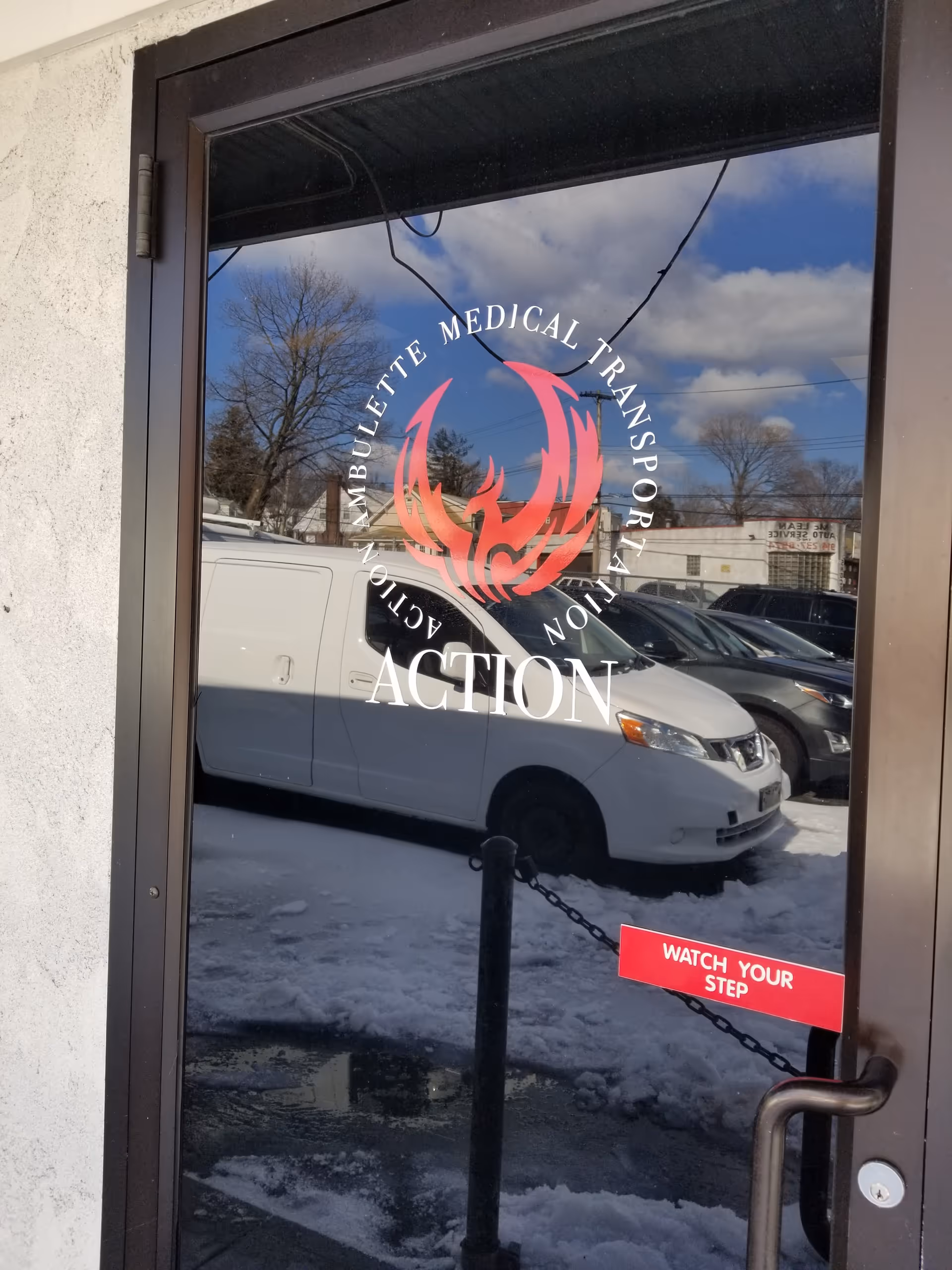 Glass entrance door bearing Action logo, reflecting vans, snow, and blue sky.