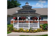 White gazebo with hanging baskets in front of a beige senior care facility.