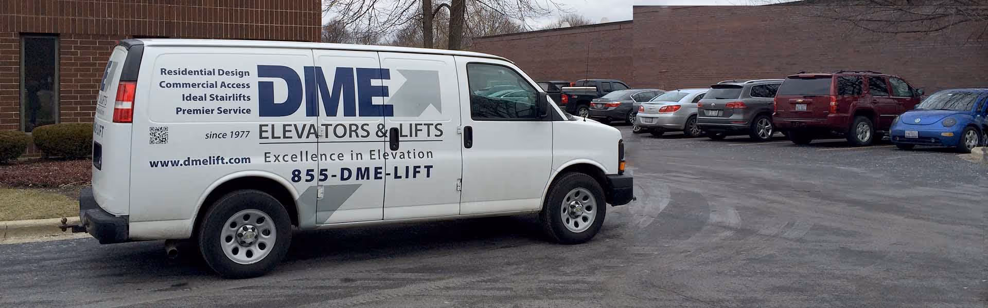 A white DME Elevators and Lifts van parked in a car lot beside a brick building.