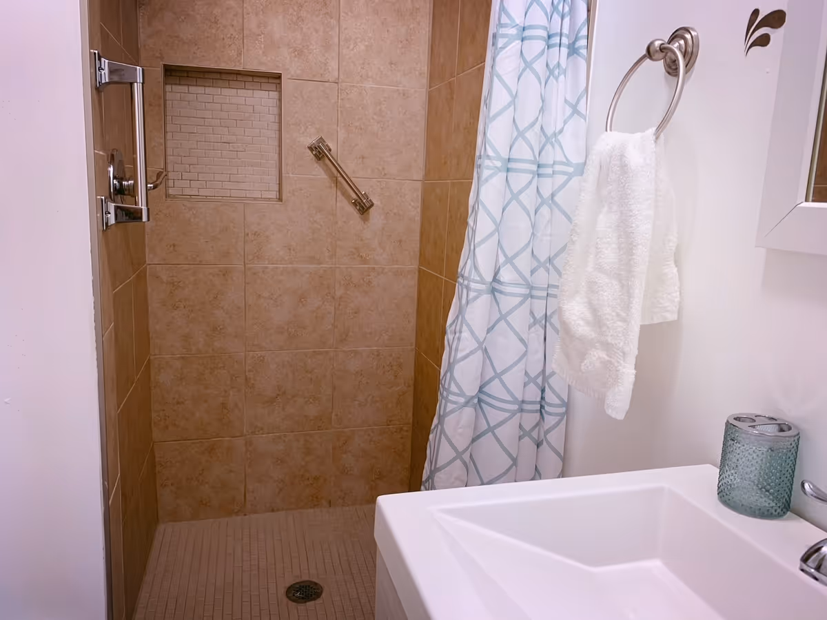 Bathroom with tiled shower, white sink, towel ring, and patterned shower curtain.