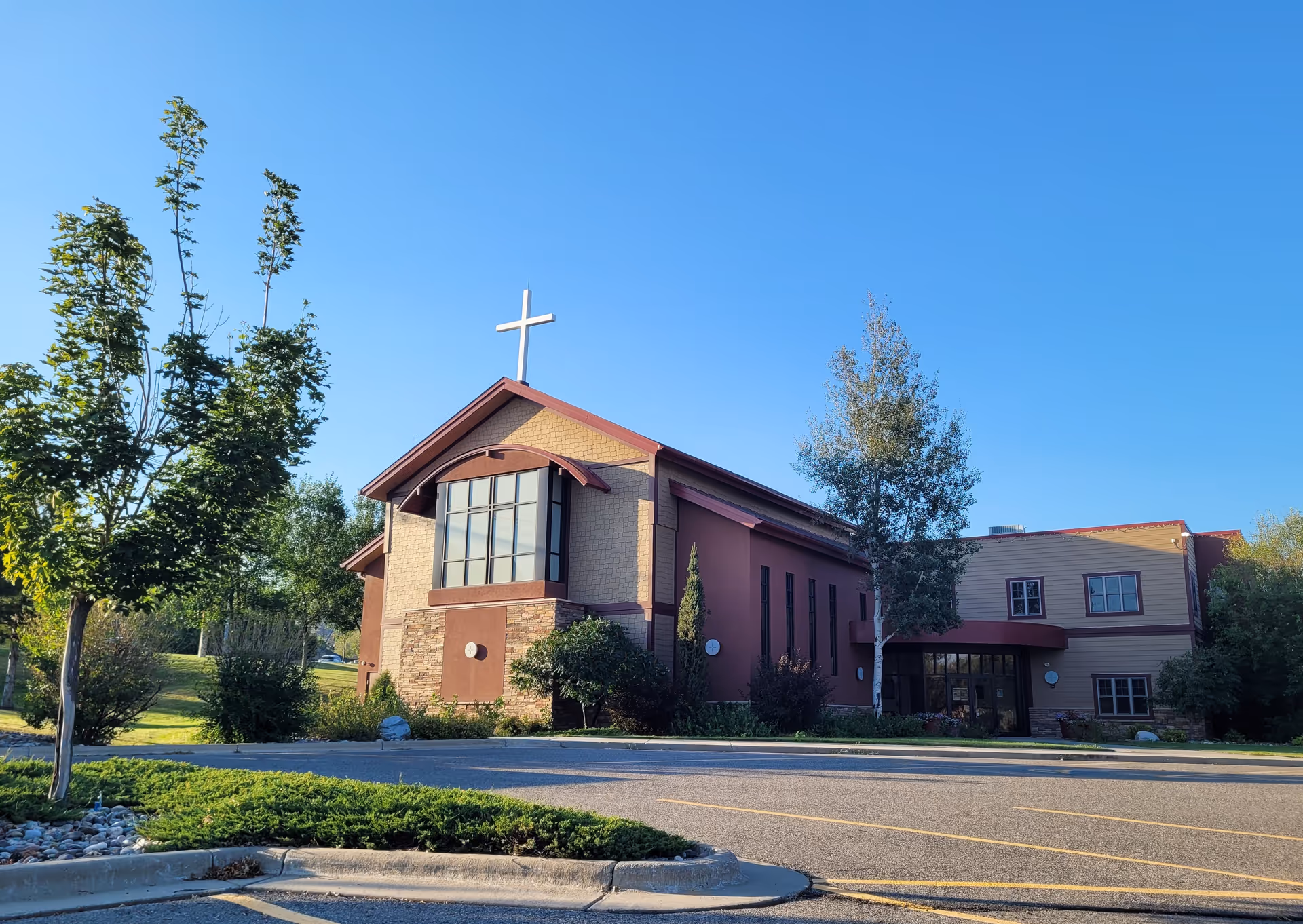 Exterior view of a church-like facility with cross atop, surrounded by trees