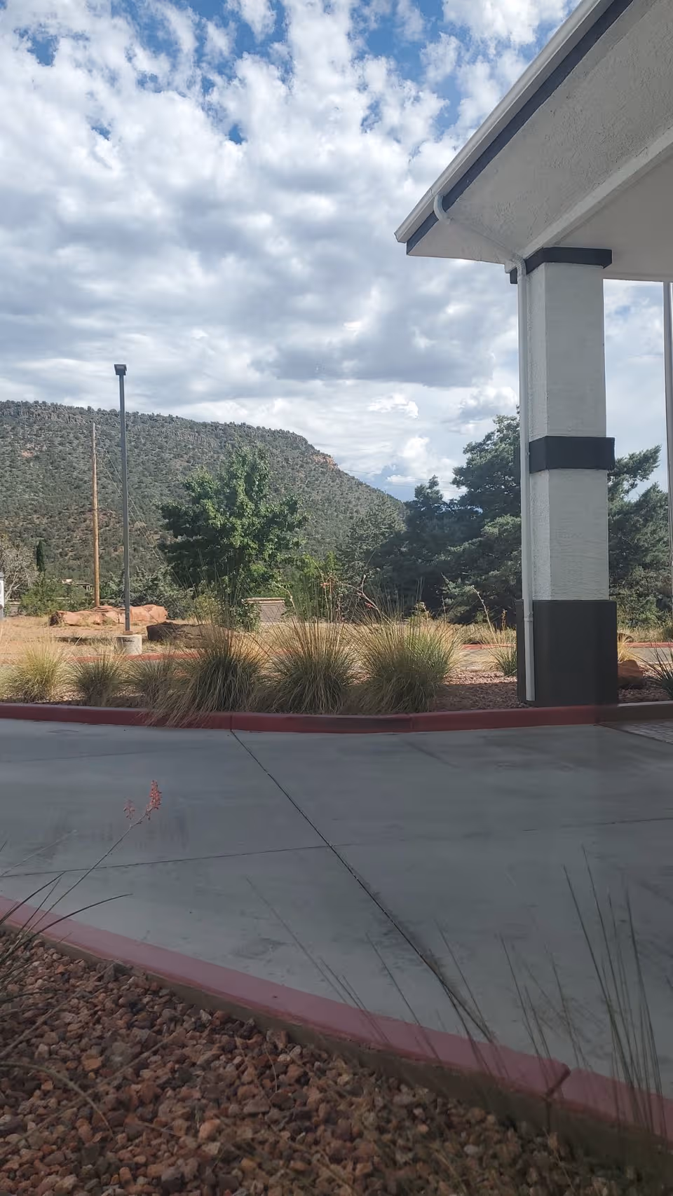 Covered building entrance with white and black pillars overlooks desert landscaping and distant hills.