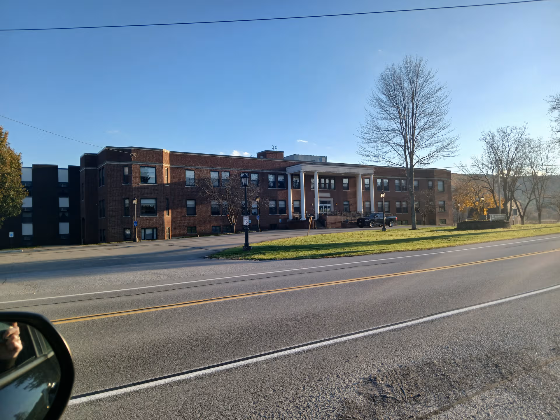 Exterior brick building with columns and a grassy median along a street.