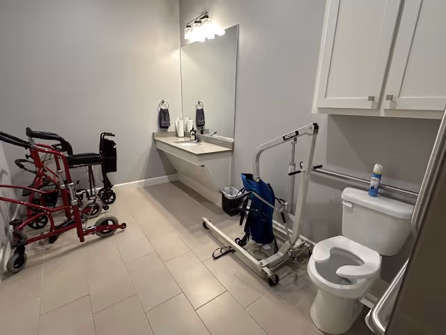 Accessible bathroom in a senior care facility with sink, mirror, toilet, and mobility aids.