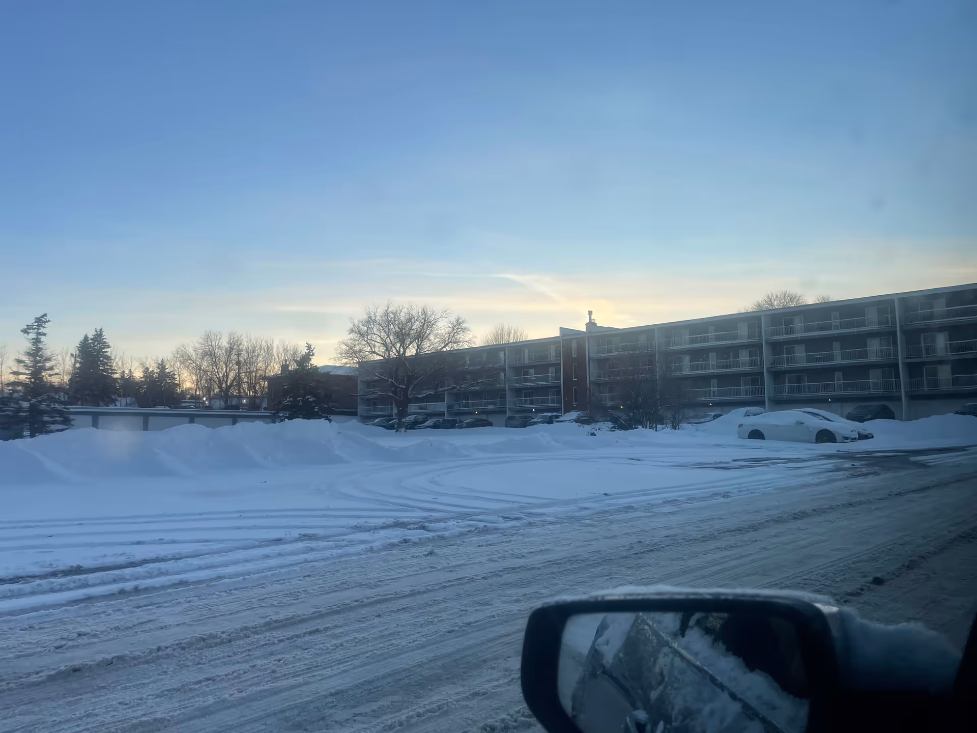 Snow-covered exterior of a senior living building with balconies and parked cars.
