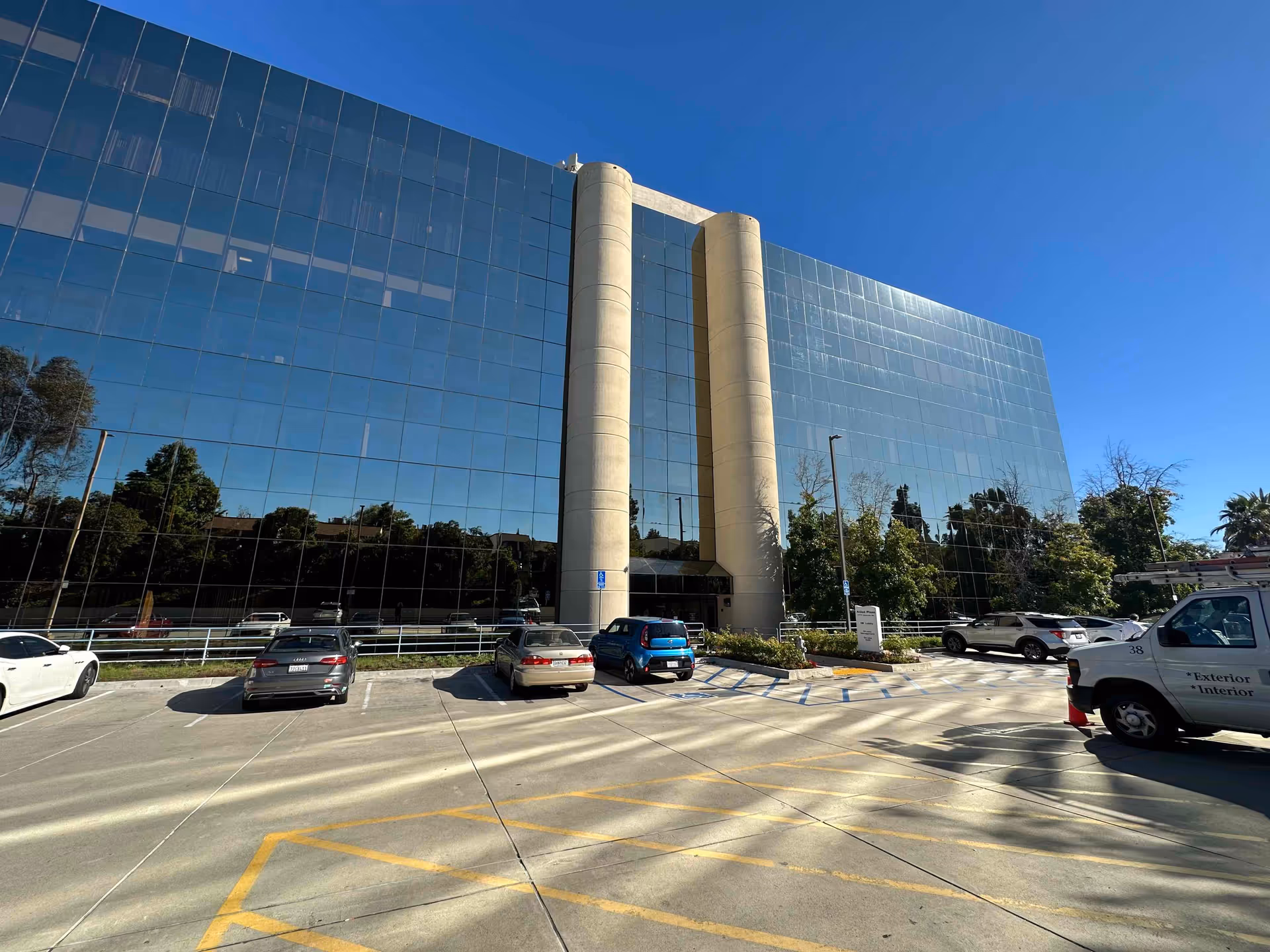 Modern glass building with a parking lot and surrounding trees