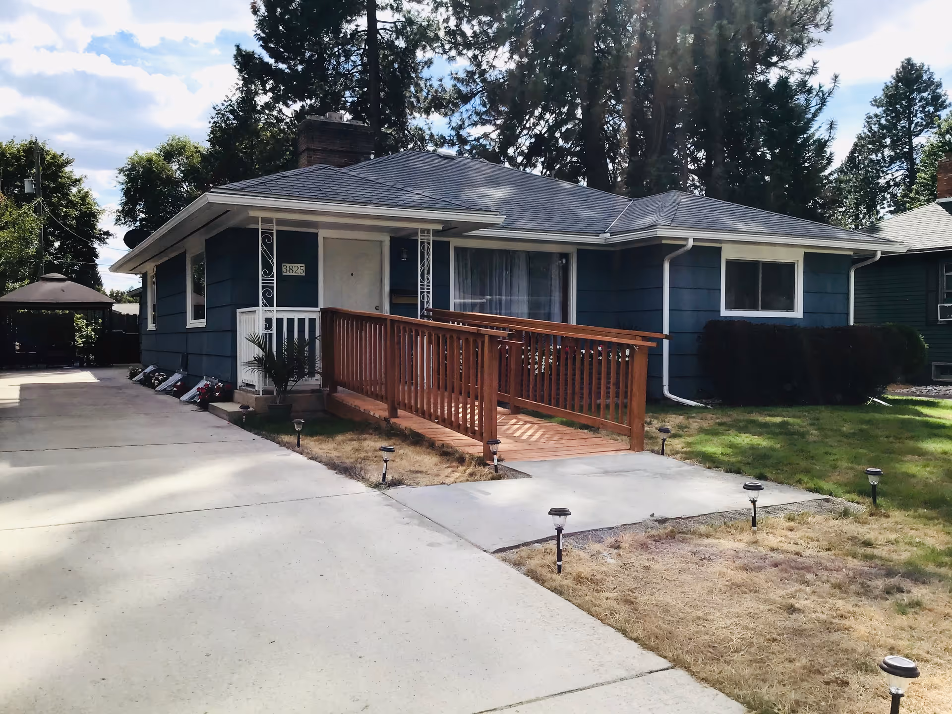 Blue single-story adult family home with wooden ramp and front walkway.